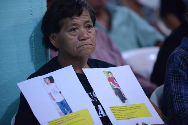 A woman held up images of her children who disappeared at Ayotzinapa during a visit by the Inter-American Commission on Human Rights on September 30, 2015 in Iguala, Mexico. (Daniel Cima/Comisión Interamericana de Derechos Humanos/Flickr/CC BY 2.0)