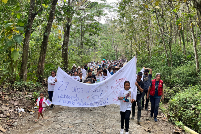 La Comunidad de Paz conmemora 27 años de resistencia pacífica, el 23 de marzo 2024. Se lleva en frente unas fotos de Edinson David. (Moira Birss) 