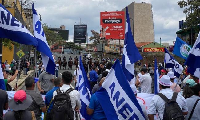 ANEP, the National Association of Public and Private Employees, faces a line of police officers on horseback during protests in San José, Costa Rica, May 1, 2023. (Isabel Villalon) 