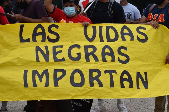 BLM protests occurred across the globe last year, a reminder that the fight for Black lives is needed everywhere. Here, a protester in the United States holds a sign proclaiming 