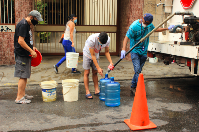 In the first weeks of the Covid-19 lockdown, people fill containers from a water truck in Caracas, Venezuela, April 4, 2020. (Edgloris Marys / Shutterstock)